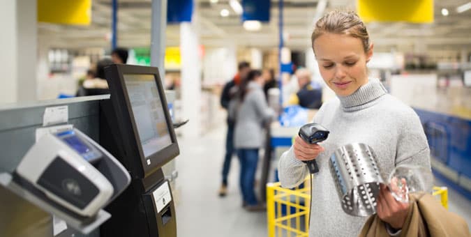 Image of woman using self-checkout scanner at kiosk